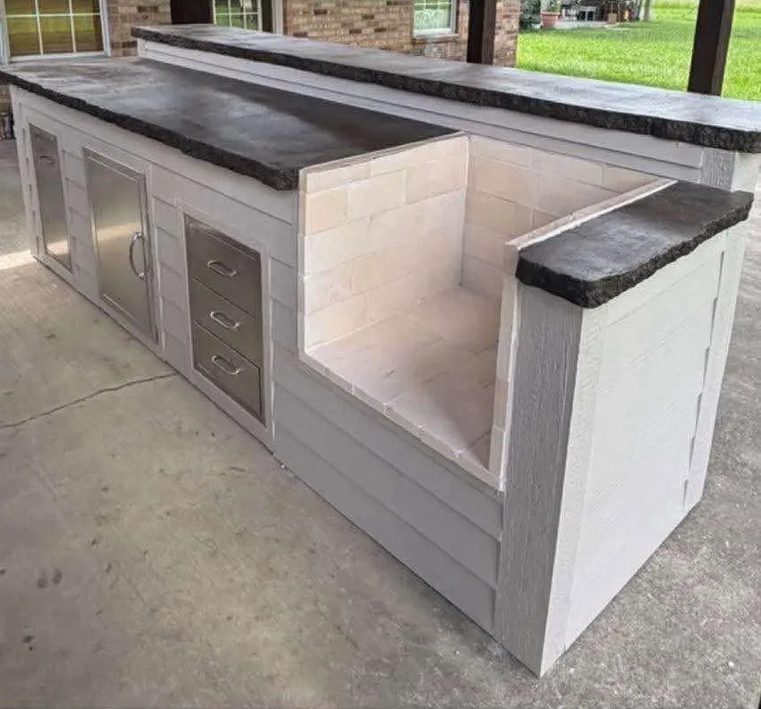 Outdoor kitchen island with pale cabinetry and dark counters beneath a covered patio.