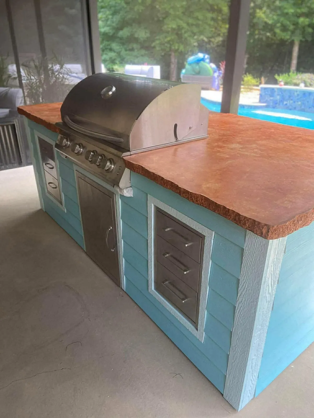 Outdoor kitchen with a built-in stainless grill, turquoise cabinetry, and a concrete counter.